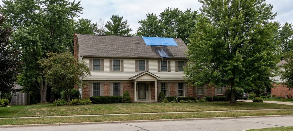 Two-story suburban home with a tarp covering a roof leak after storm damage